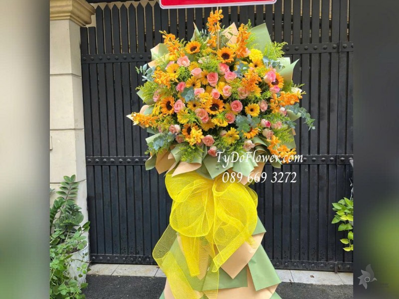 KCM1025849 KỆ HOA CHÚC MỪNG HỘI NGHỊ Thiết kế hoa hồng Lạc Thần, lan Mokara, Hướng Dương, Đồng Tiền Vàng trên nền giấy mỹ thuật cao cấp