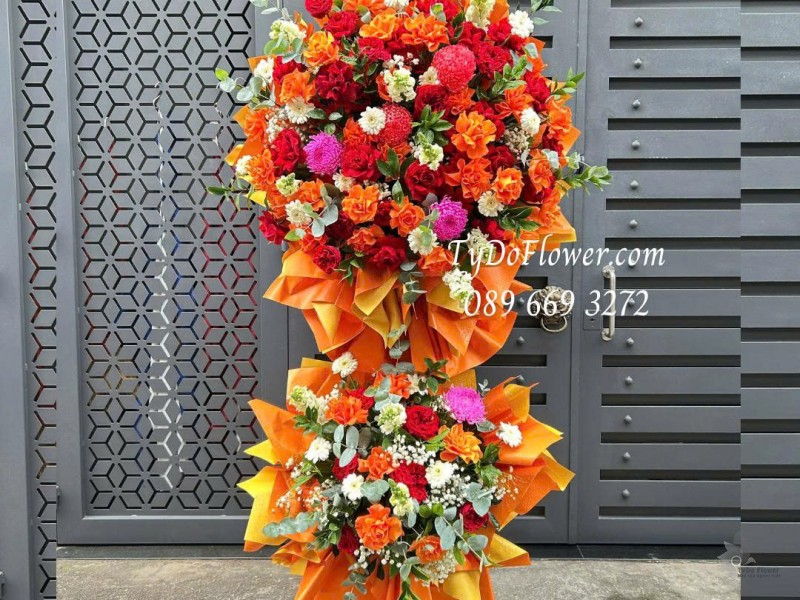 KCM0126031 KỆ HOA CHÚC MỪNG HỘI NGHỊ Thiết kế tông màu đỏ cam, hoa hồng gấp cánh, đồng tiền, cúc mẫu đơn trên nền giấy mỹ thuật cao cấp