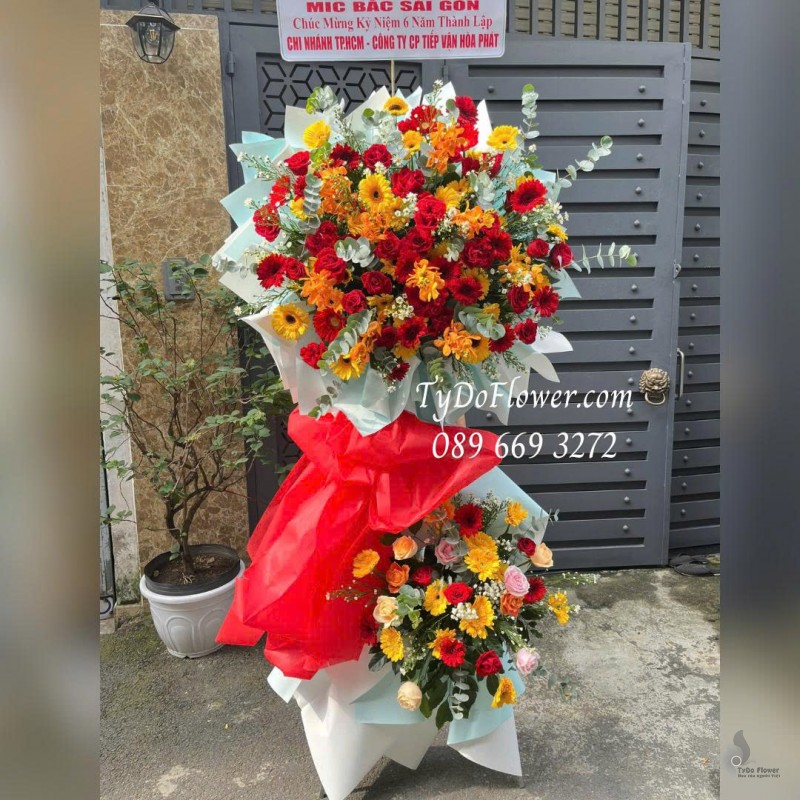 KCM0126030 KỆ HOA CHÚC MỪNG KỶ NIỆM NGÀY THÀNH LẬP Thiết kế tông màu đỏ vàng, hoa hồng, đồng tiền, lan mokara