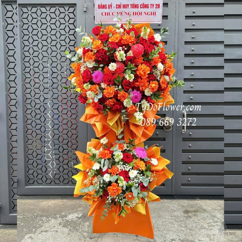 KCM0126031 KỆ HOA CHÚC MỪNG HỘI NGHỊ Thiết kế tông màu đỏ cam, hoa hồng gấp cánh, đồng tiền, cúc mẫu đơn trên nền giấy mỹ thuật cao cấp